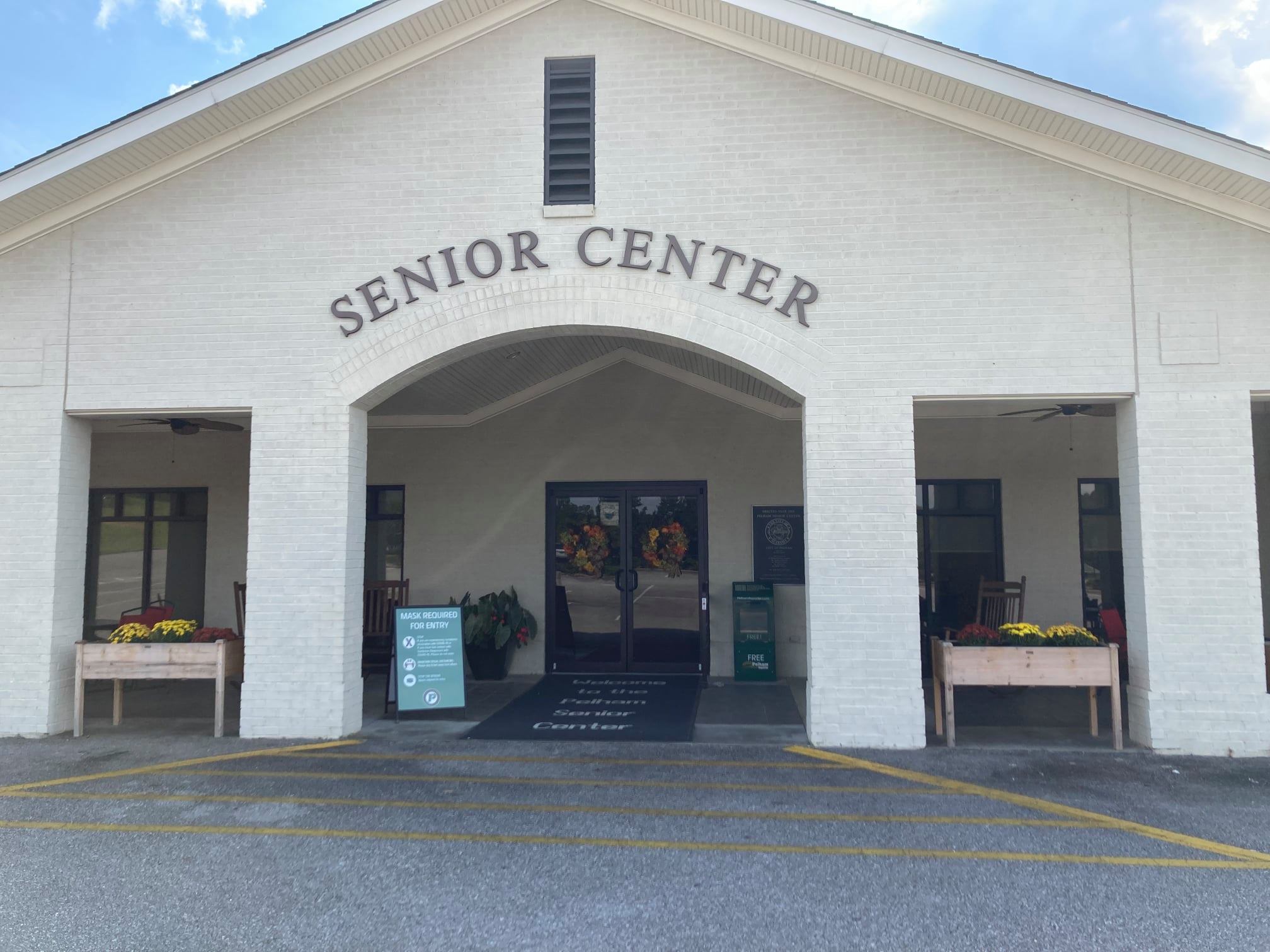 Front of Senior Center building. Four flower beds with mums. 