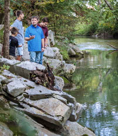A man and three boys explore the area along the banks of Bishop Creek in Pelham City Park.
